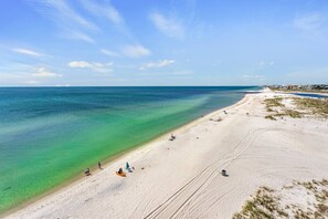 Ein Strand mit klarem türkisblauem Wasser, einem Sandstrand und einigen Personen sowie Strandliegen.