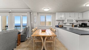 A compact kitchen with white cabinets, a wooden dining table, and a view of the ocean through the sliding glass doors. - Pinnacle Port A533 (Panama City Beach)