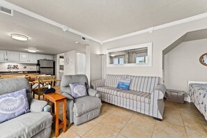 Een compacte woonruimte met een kitchenette, een gestreepte bank en een eethoek.