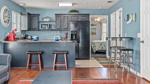 A modern kitchen with dark cabinets, a black refrigerator, and a microwave. There are two stools and a bar stool near the kitchen counter. - Fun and Sun Vacation Townhome (Panama City Beach)