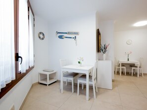 Ett rent, vitt rum med ett matbord och stolar, en liten hylla och en skylt som hänger på väggen med texten "STRANDHUS".