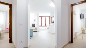 A spacious hallway with a high ceiling, leading to a living area with a TV, seating, and a window.