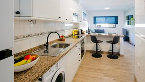 Une cuisine moderne avec des armoires blanches, un comptoir en granit, un lave-linge intégré et un petit îlot central doté de tabourets de bar.