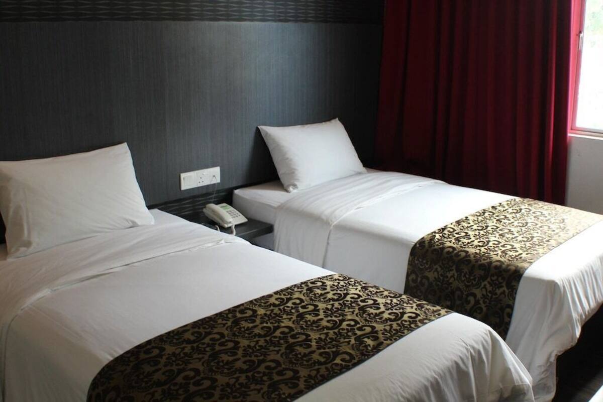 A hotel room with two beds, each with white linens and a patterned bedspread. There is a telephone on the nightstand beside the beds.