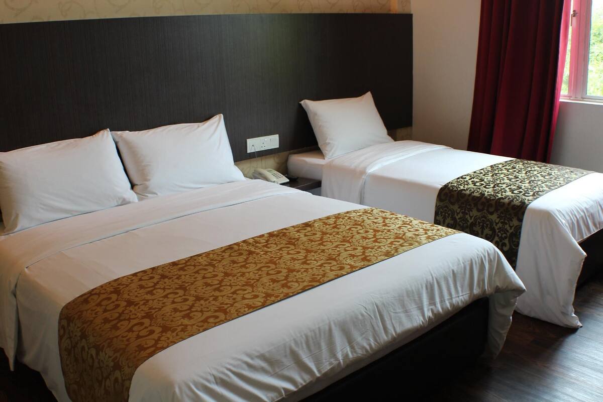 A hotel room with two beds, each with white bedding and a patterned runner. There is a nightstand with a phone between the beds.