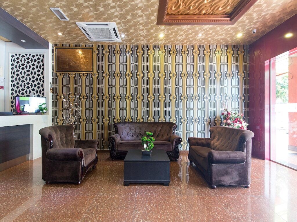 A lobby with patterned wallpaper, a reception desk, and three brown armchairs around a black coffee table.