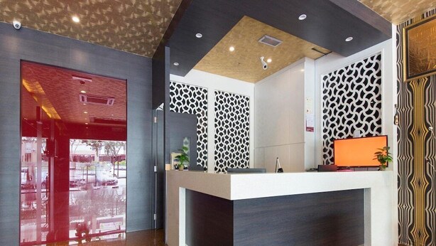 A reception desk with a modern design, a patterned wall, and a red door. - Hotel Rosmerah (Malacca City)