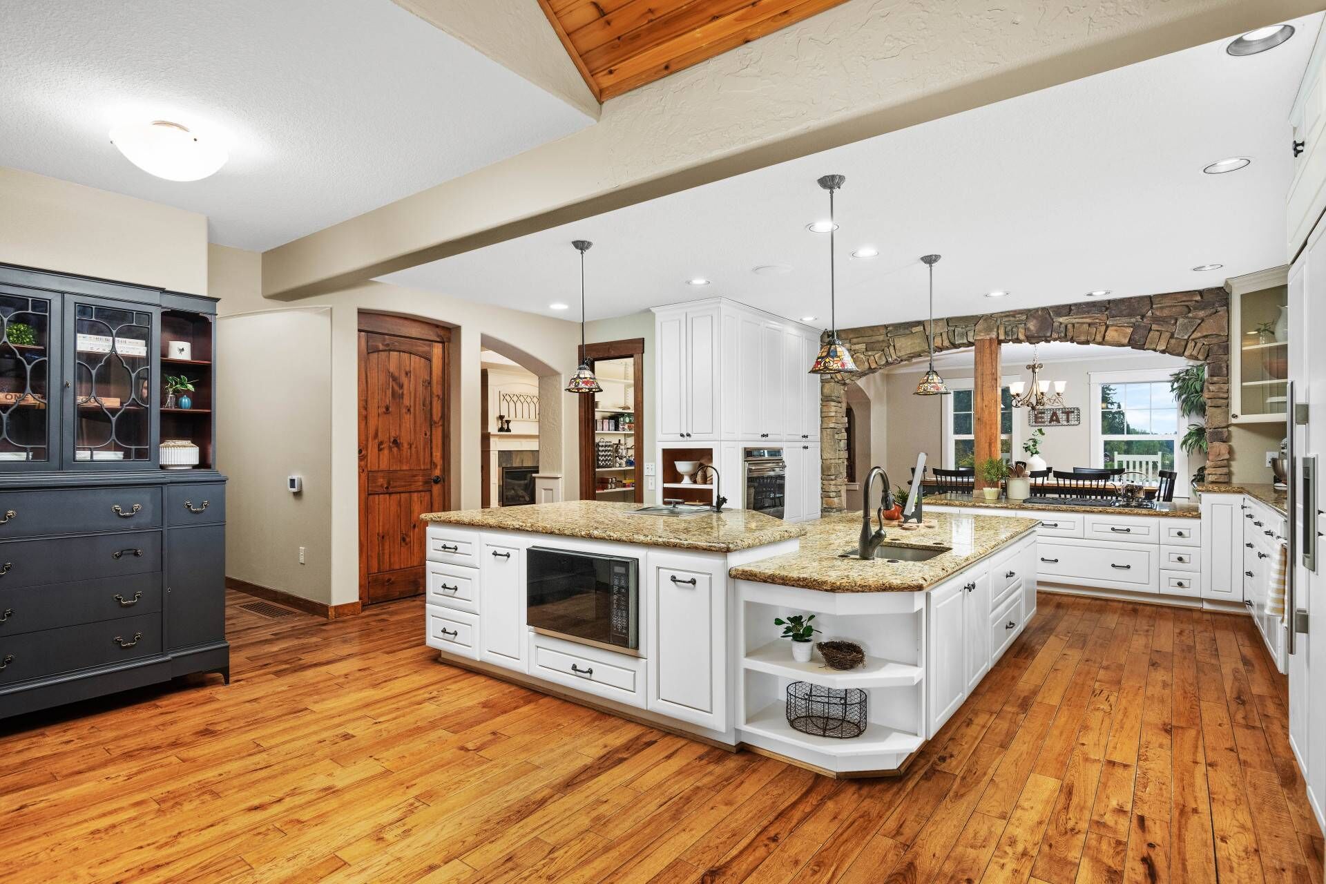 A spacious kitchen with white cabinetry, a granite countertop island, and a wooden floor.