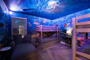 A room with bunk beds, a couch, and an aquarium wall.