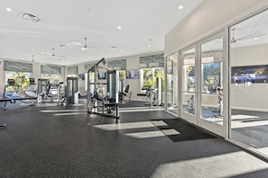 A modern gym with treadmills, weight machines, and a large window offering a view of the outdoors.