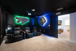 A room with a Star Wars-themed wall, a ceiling projector, and a seating area with black leather chairs.