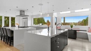 Una cocina moderna con una isla grande, taburetes de bar y vistas al exterior a través de amplios ventanales.