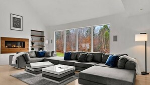 A modern living room with a sectional sofa, a fireplace, and a large window with a view of trees.