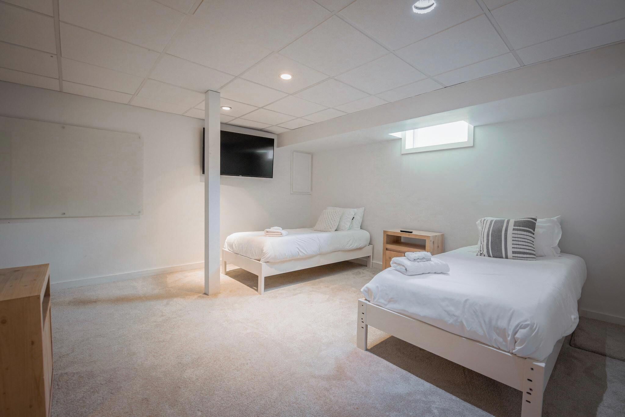A bedroom with two beds, a TV mounted on the wall, and a window providing natural light.