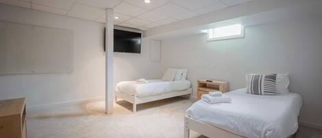 A bedroom with two beds, a TV mounted on the wall, and a window providing natural light.