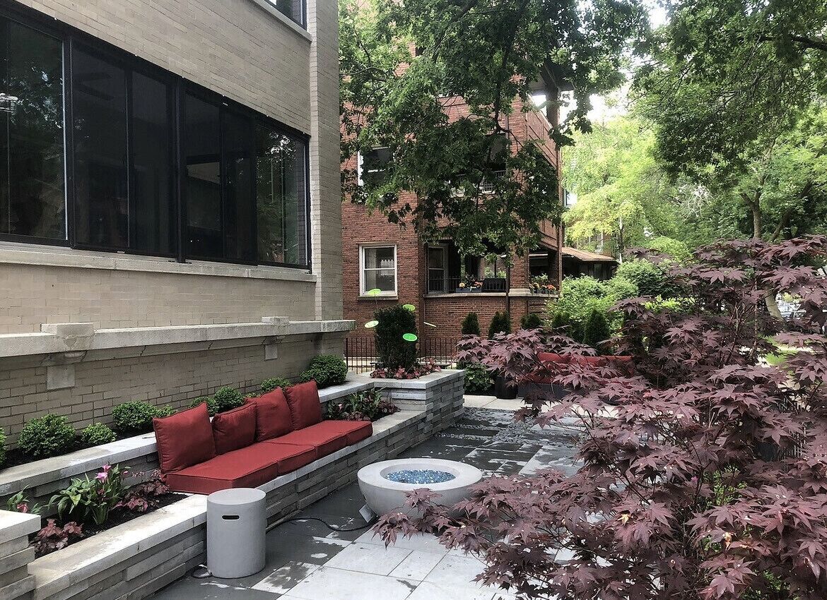 Une cour avec un espace extérieur agrémenté de sièges rouges, un foyer et un bâtiment en briques doté de grandes fenêtres.