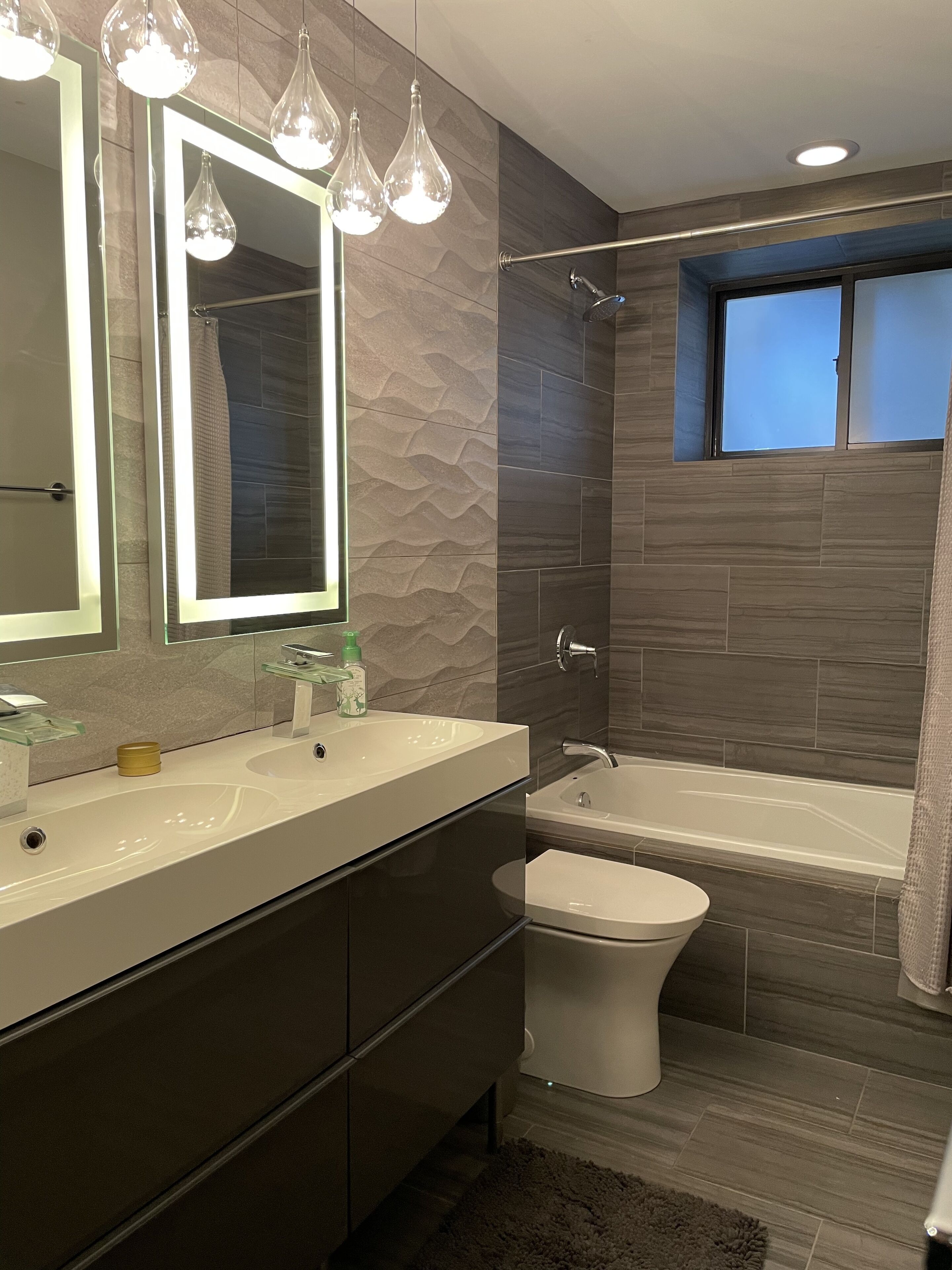 A modern bathroom with a large mirror, two sinks, a shower, and a toilet.