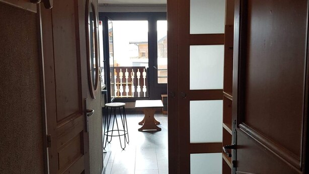A hallway with a wooden door on the right, a small table with chairs, and a view of the outside through a window. - LES Glaciers Studio 25m2 (Les Belleville)