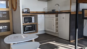 A compact kitchen with white cabinets, a microwave, a toaster, and a sink. There is a small table with a menu on it. - LES Glaciers Studio 25m2 (Les Belleville)