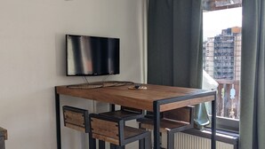 A modern room with a wooden desk, a flat-screen TV, and a view of a cityscape through a window with curtains. - LES Glaciers Studio 25m2 (Les Belleville)