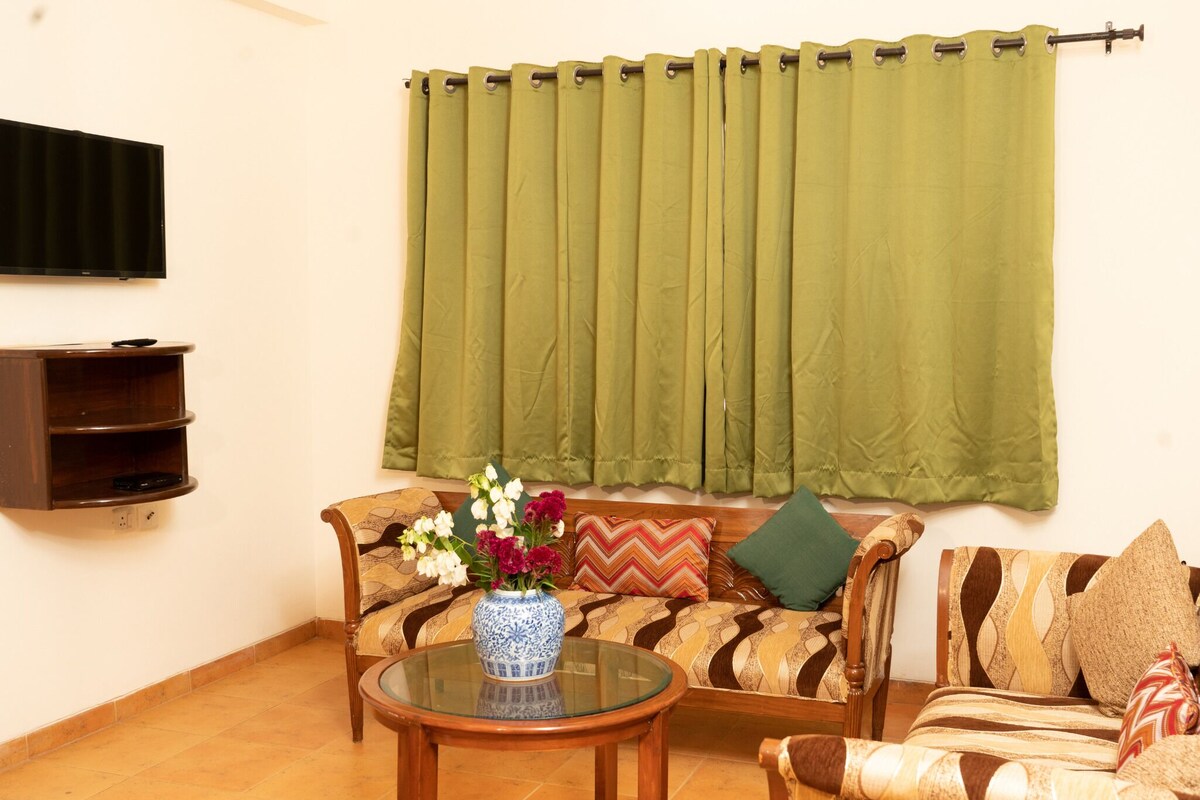 A living room with a sofa, a coffee table, and a flat-screen TV mounted on the wall.