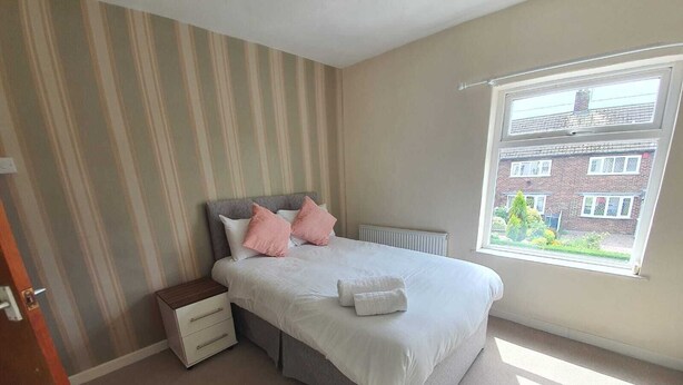 Une chambre à coucher avec un lit, un radiateur, une fenêtre donnant sur un immeuble en briques et un mur à rayures.