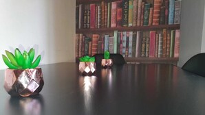 Une table sur laquelle sont posés trois pots métalliques contenant des plantes vertes, le tout placé devant une bibliothèque remplie de livres.