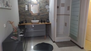 A modern bathroom with a stone backsplash, a large mirror, a sink, and a shower area. - Appartement Quartier Calme (Perpignan)