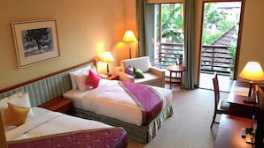 Une chambre d’hôtel avec deux lits, un bureau, une chaise et un balcon donnant sur un espace verdoyant.