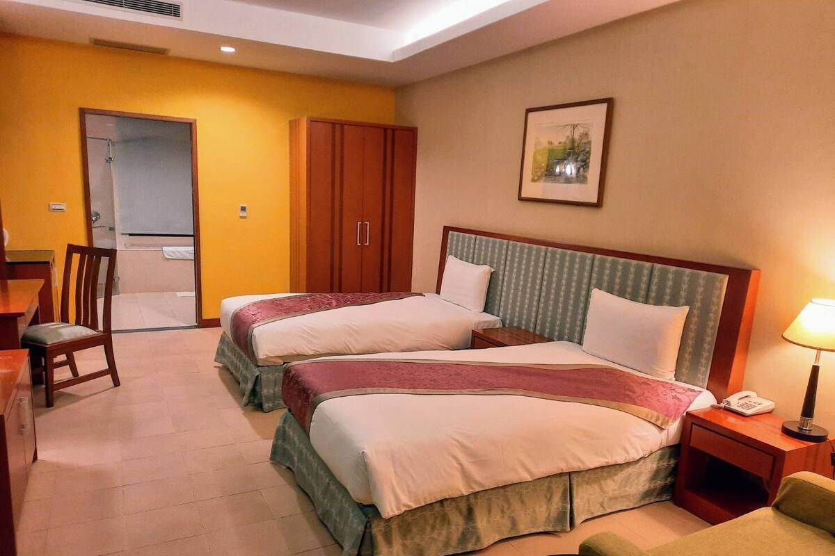 A hotel room with two beds, a desk, a chair, and a wardrobe.