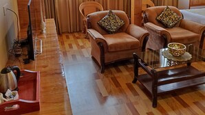 A wooden-paneled room with two leather armchairs, a glass coffee table, and a wooden desk with a kettle. - Mash Denzong Shiron (Gangtok)