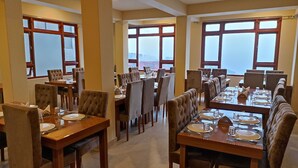 A restaurant with multiple dining tables and chairs, large windows, and a high ceiling. - Mash Denzong Shiron (Gangtok)