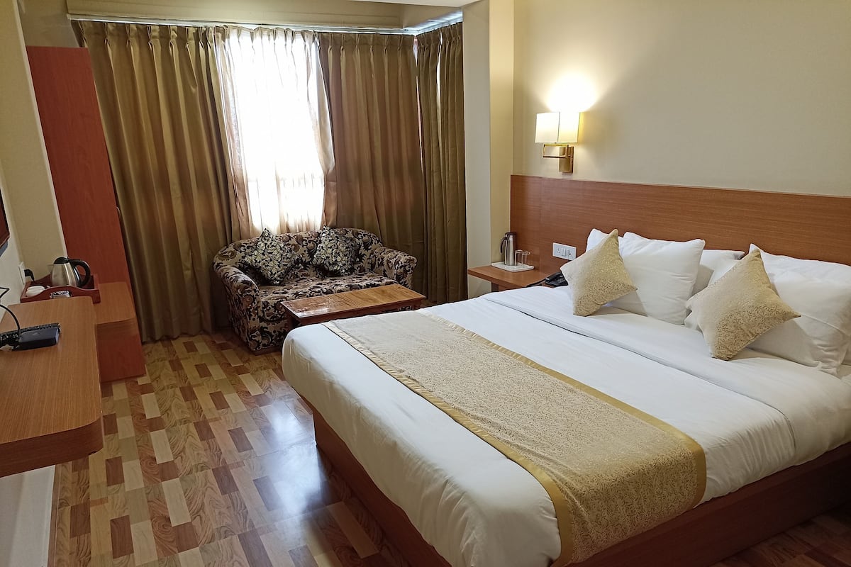 Quarto de hotel com uma cama grande, um sofá, uma mesa de centro de madeira e uma mesa de cabeceira com abajur.
