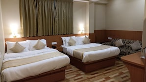 A hotel room with two beds, a wooden headboard, a small desk, and a patterned sofa. - Mash Denzong Shiron (Gangtok)
