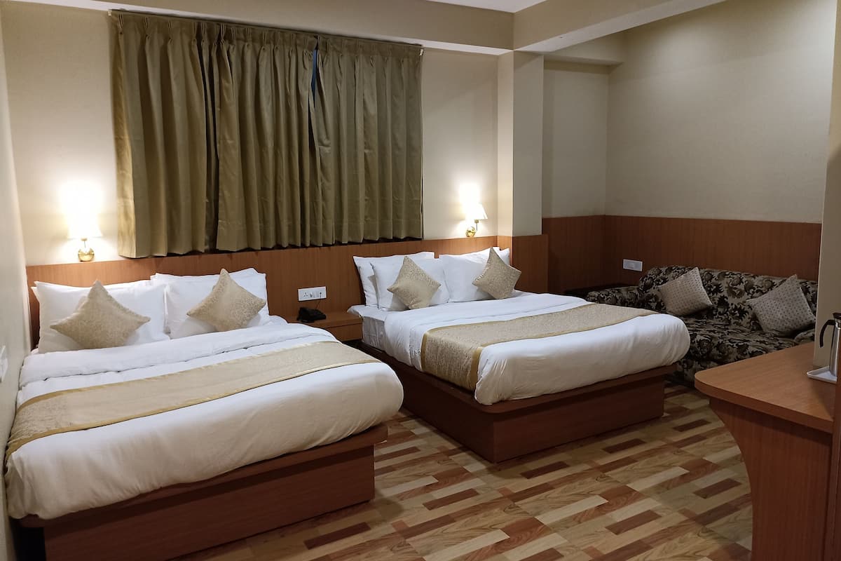 Quarto de hotel com duas camas, cabeceira de madeira, escrivaninha pequena e sofá estampado.