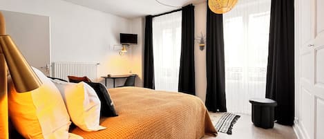 A neatly arranged hotel room with a large bed, a small table, a chair, and a television mounted on the wall.