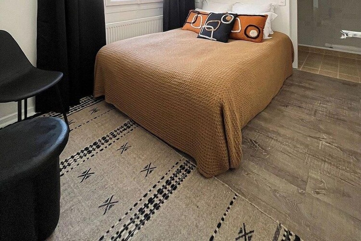 Une chambre à coucher avec un lit, une chaise, une fenêtre avec des rideaux, un luminaire au plafond et une porte.