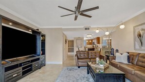 A modern living room with a large flat-screen TV, leather sofas, a coffee table, and a ceiling fan. - 4541 Bay Beach Ln #345 (Fort Myers Beach)