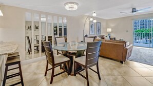 A modern dining area with a round glass table and dark wooden chairs, a brown leather sofa, and a ceiling fan. - 4541 Bay Beach Ln #345 (Fort Myers Beach)