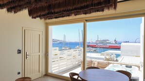 A balcony with a view of the sea, a hot tub, and a dining area with chairs and a table. - LIFE SUITES (Mykonos)