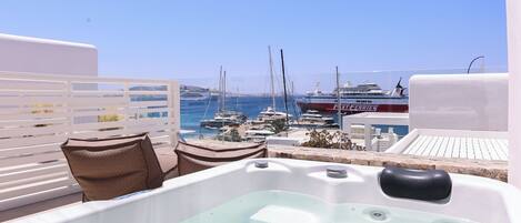 A rooftop pool area with a hot tub, lounge chairs, and a view of boats and yachts at a marina.