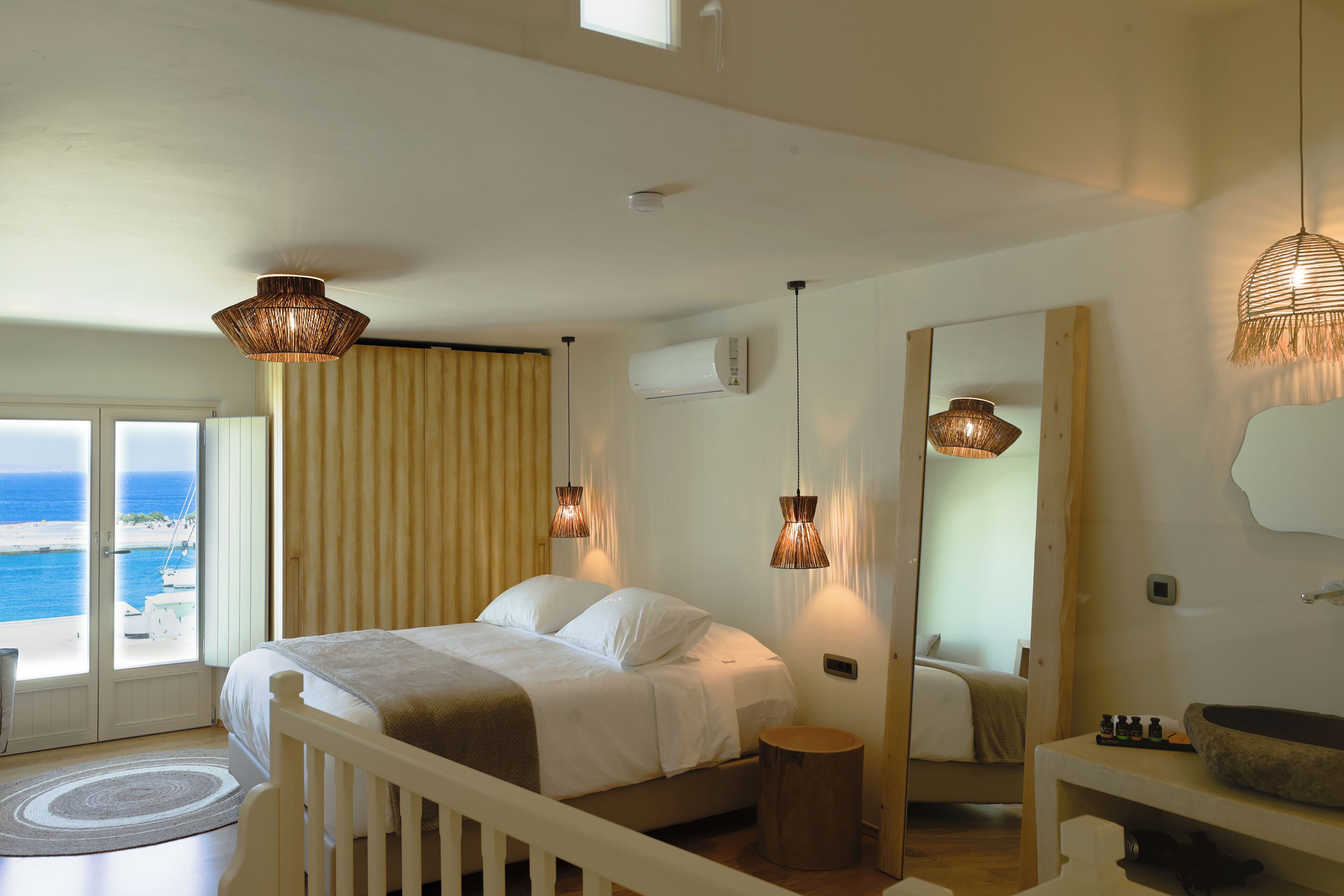 A bedroom with a bed, bedside table, and a view of the sea through a sliding door.