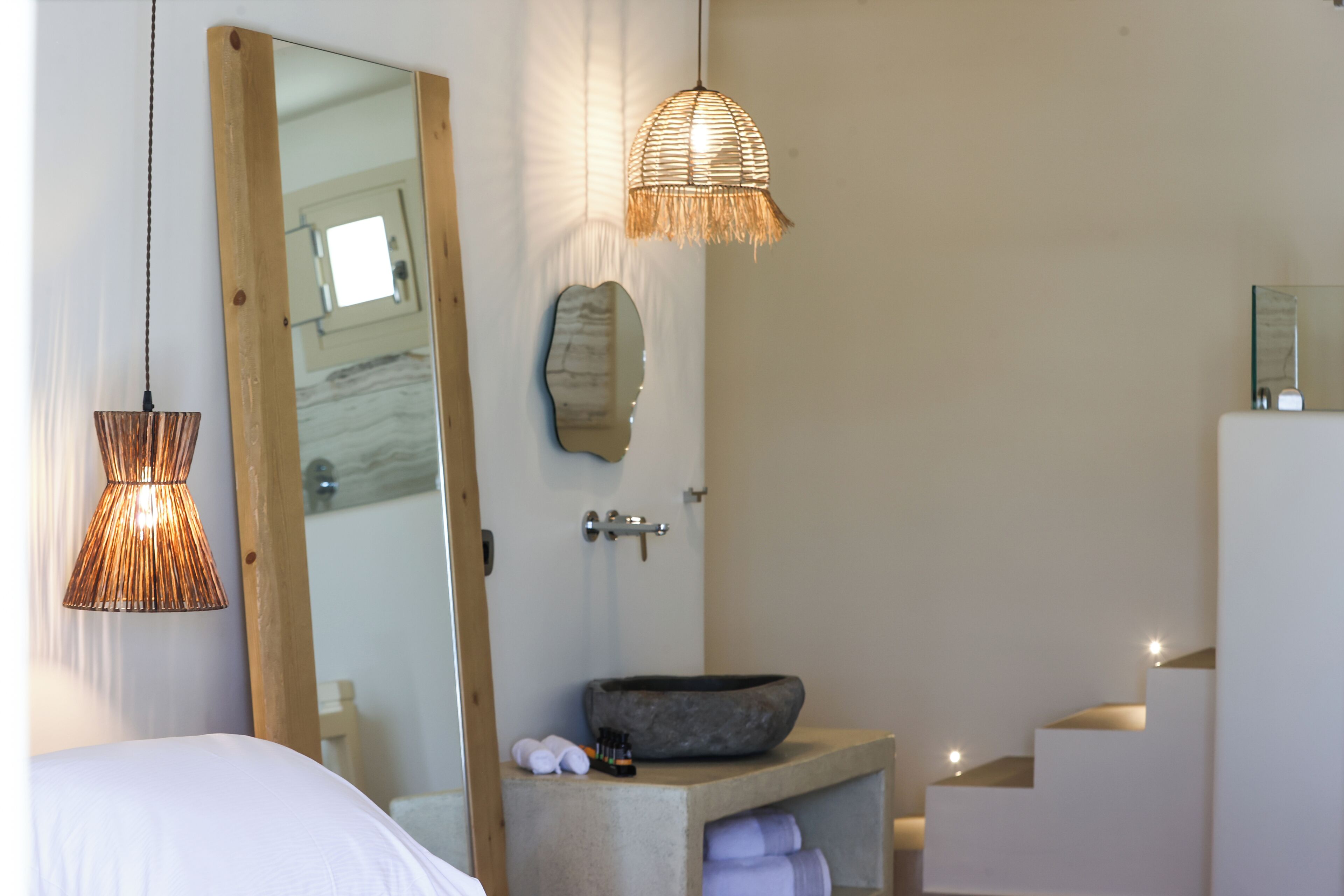 A modern bathroom with a large mirror, a stone sink, and a built-in bench.
