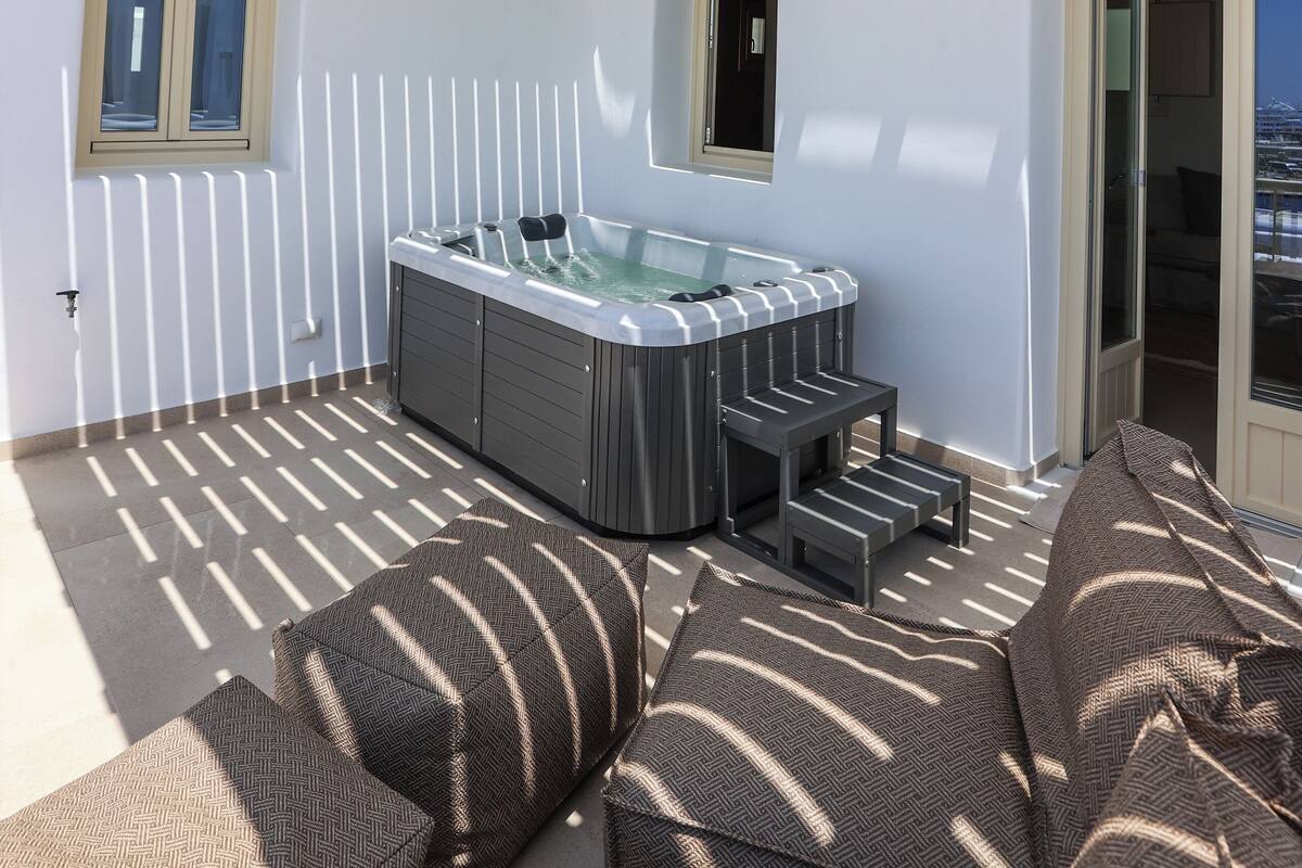 A sunlit outdoor area with a hot tub, seating, and a view of the sea.
