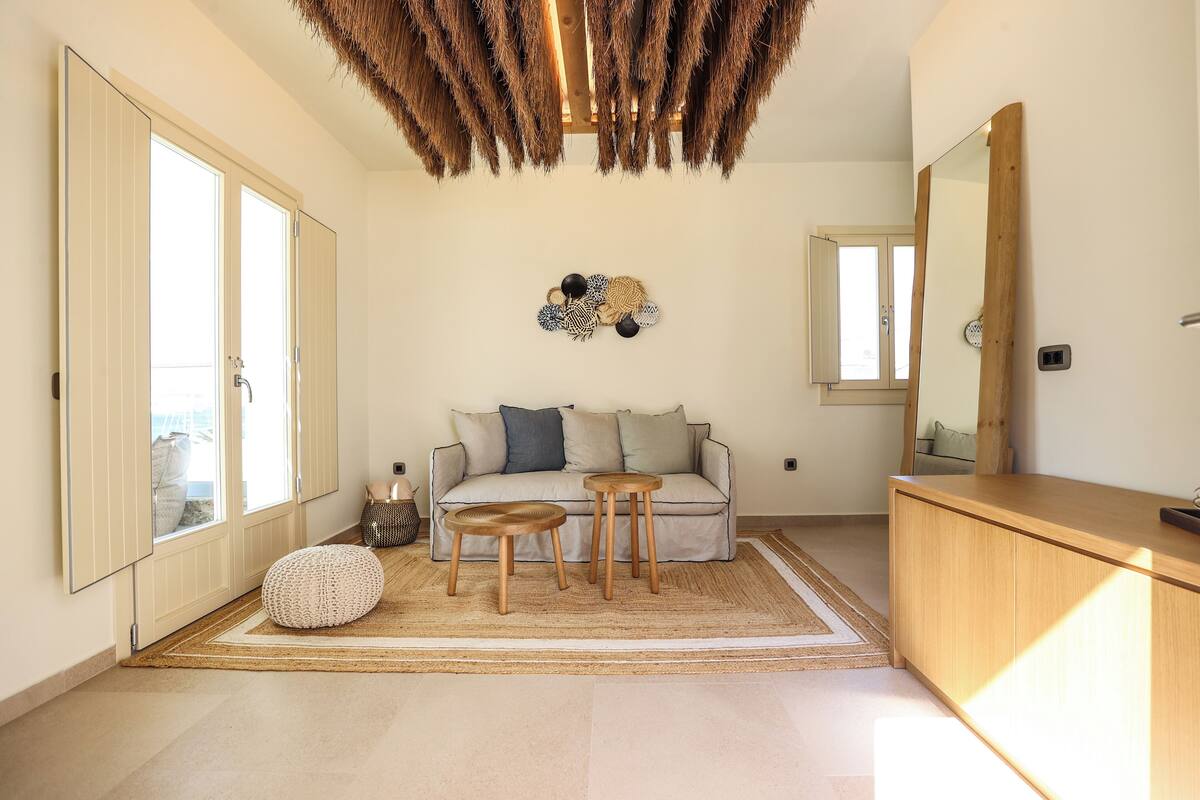 A modern living room with a sofa, two wooden stools, a woven rug, and a large mirror.