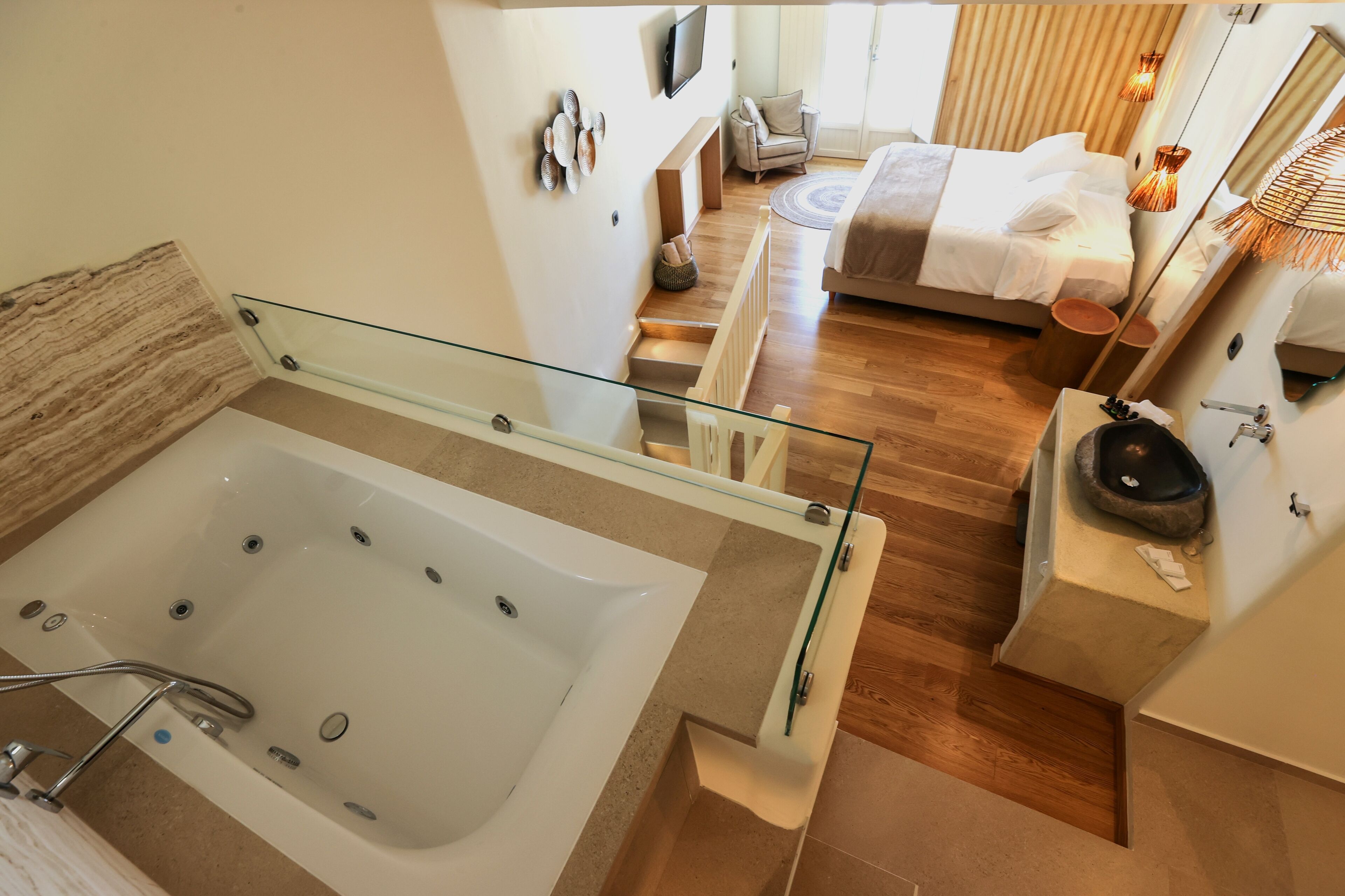 A modern bathroom with a glass-enclosed bathtub, wooden flooring, and a visible staircase leading to a bedroom.