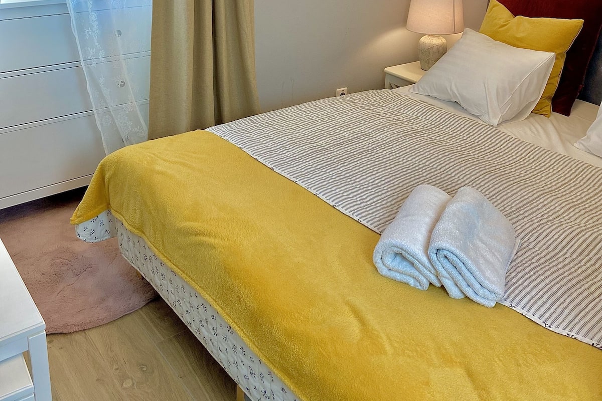 Een netjes ingerichte slaapkamer met een bed, nachtkastje, lamp en ingelijste foto's aan de muur.
