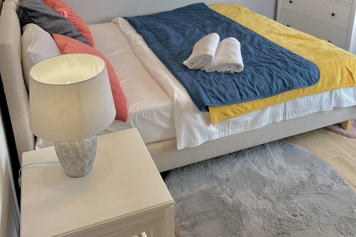 Een keurig opgemaakt slaapkamer met een bed, nachtkastje, lamp en een klein dressoir.