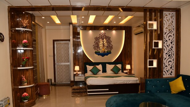 A modern bedroom with a bed, a sofa, a decorative wall, and a wooden cabinet. - Hotel Buddha International (Patna)