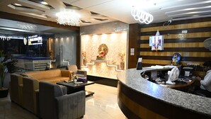 A hotel reception area with a marble counter, sofas, and a decorative Buddha statue. - Hotel Buddha International (Patna)